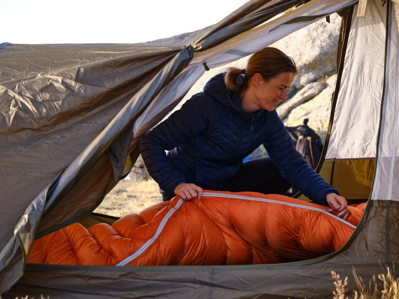 Femme qui plie un sac de couchage dans une tente