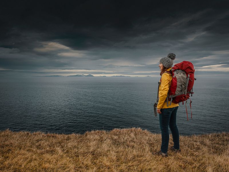 Femme qui contemple la mer en portant un sac à dos de randonnée