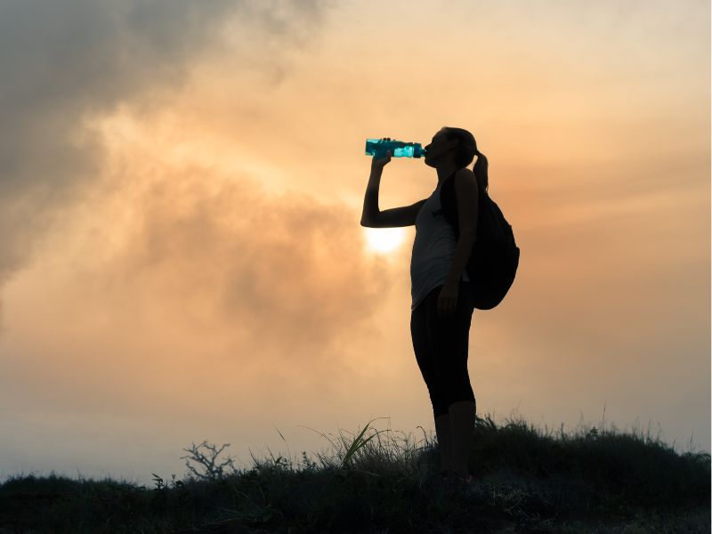 Randonneuse qui boit dans une bouteille au crépuscule