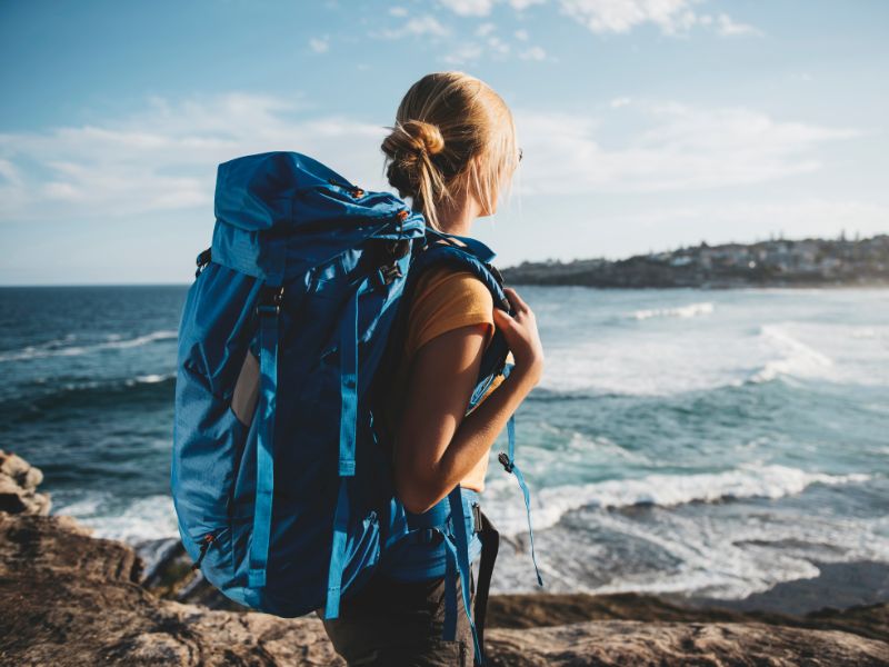 Femme qui porte un sac à dos de randonnée face à la mer