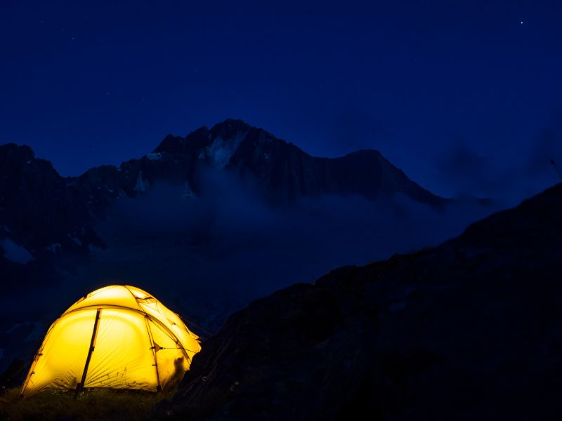 Tente éclairée durant la nuit face aux montagnes